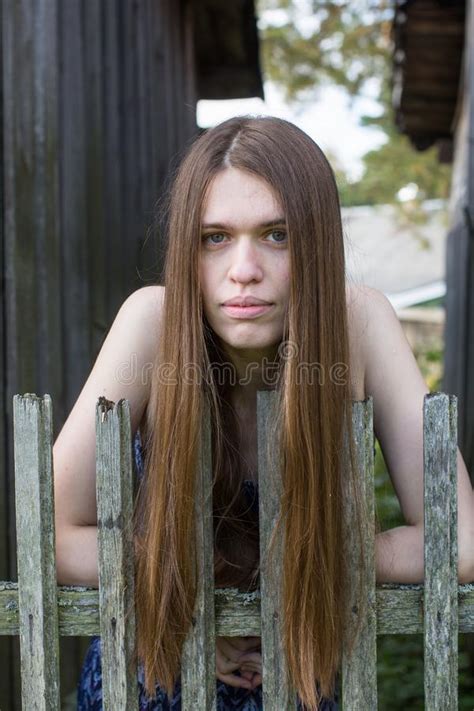 Long Haired Girl Stands Near A Wooden Village Fence Stock Image