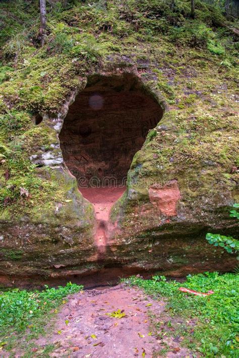 Sandstone Cliff With Dark Cave Entrance In Green Forest Stock Photo