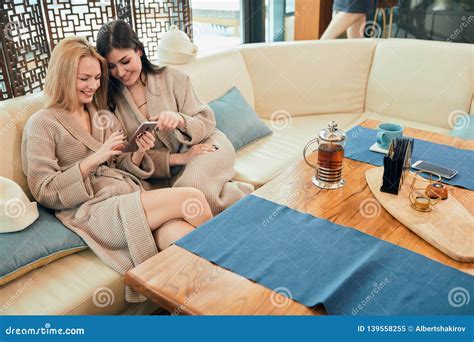 Relaxed Diverse Friends In Bathrobes Sitting At Lounge Zone Of