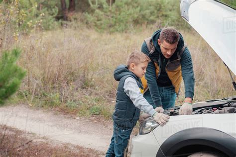 Father And Son Repairing Car Engine Together In Forest Stock Photo