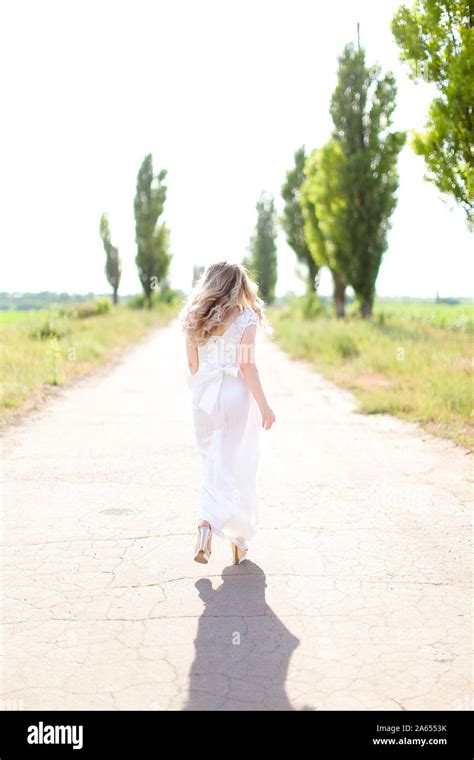 Back View Of European Woman Wearing White Dress Walking On Road Stock