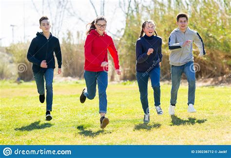 Happy Teenage Friends Chasing Each Other On Green Meadow Stock Photo