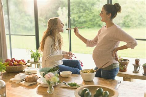 Pregnant Women Cooking And Tasting Food At Table Stock Photo