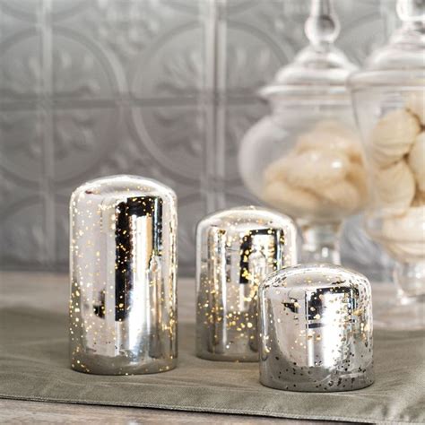 Three Silver Candles Sitting On Top Of A Table Next To A Vase Filled