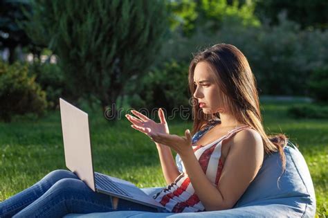 Young Cute Girl With Laptop Sit On Bean Bag In Garden Or Park On