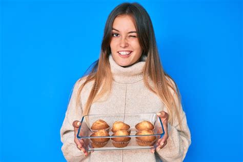 Beautiful Caucasian Woman Holding Homemade Muffins Winking Looking At The Camera With Expression