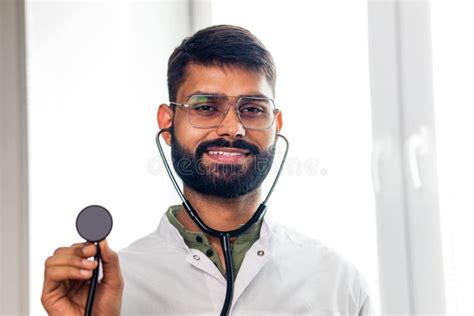 Portrait Of Male Indian Doctor Wearing White Coat In Clinic Office