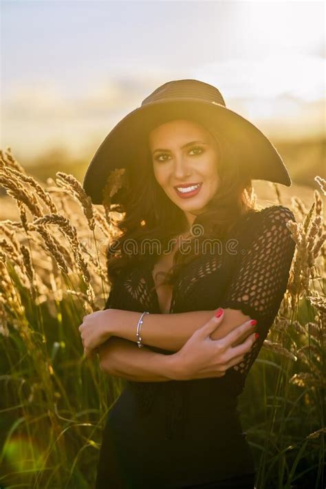 A Brunette Woman With Hat Poses In The Grass At Sunset Stock Image