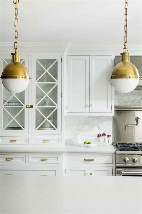 Luxurious kitchen in gold and black boasting a black kitchen island with white quartz and a set of gold and black counter stools illuminated by inset black flat front kitchen cabinets accented with matte black hardware is topped with a quartz countertop holding glass and brushed gold shelves. kitchen island light fixtures that completely change your ...