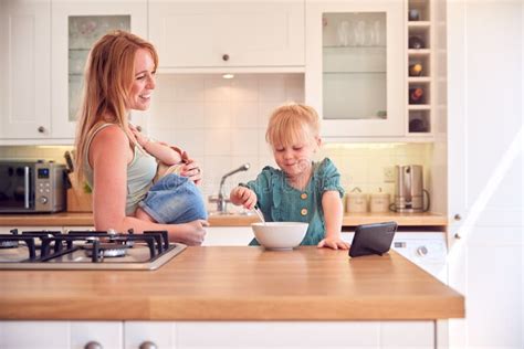 Girl At Kitchen Counter Eating Breakfast Watching Mobile Phone Whilst