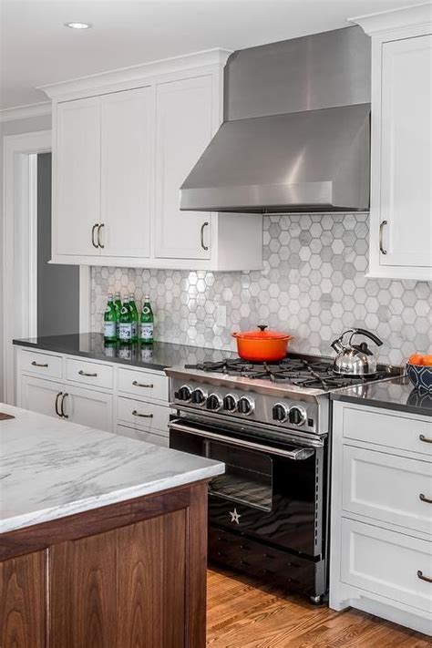 If you want a really warm, soft look, consider a pastel pink or dusty rose tile for your backsplash. A stainless steel hood mounted against large hexagon ...