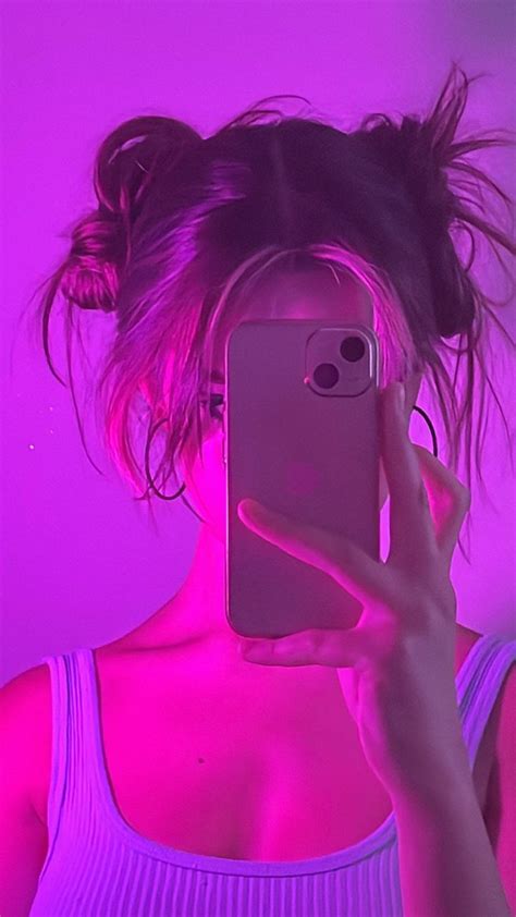 a woman taking a selfie with her cell phone in front of her face and pink light behind her