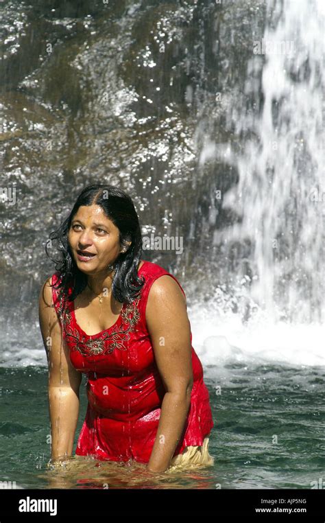 Corpulent Young Indian Woman Bathing Outdoors Under Waterfall Dressed In Red Singlet Stock
