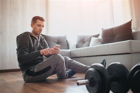 Young Ordinary Man Go In For Sport At Home Has Rest With Sitting On Floor And Use Smartphone