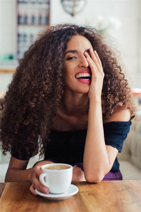 portrait of a happy curly woman having coffee in a restaurant by stocksy contributor