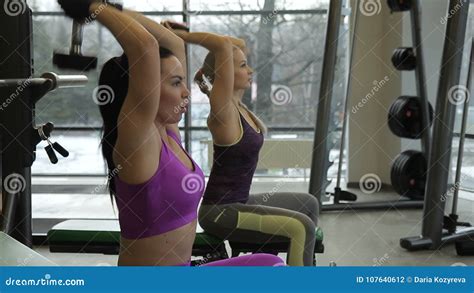 Two Female Sportswomen Are Doing Back Dumbbell Raises Sitting On The Benches In The Gym Stock