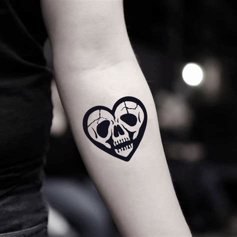 A Womans Arm With A Skull And Heart Tattoo On The Left Side Of Her Arm