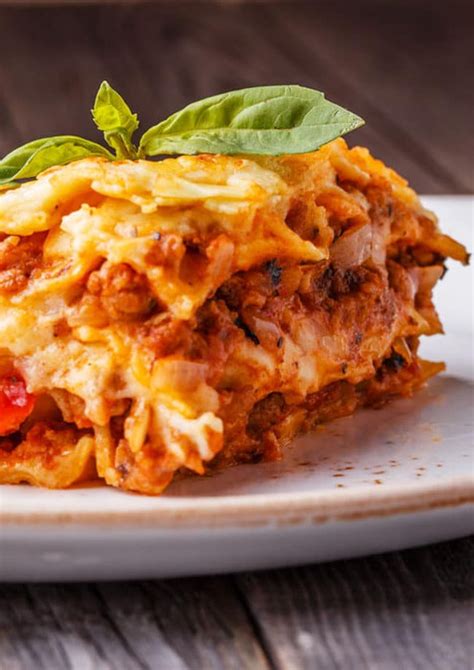 A White Plate Topped With Lasagna Covered In Meat And Cheese Garnished