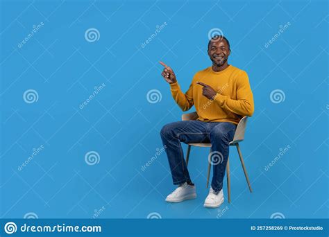 Positive Black Man Sitting On Chair Pointing At Copy Space Stock Image