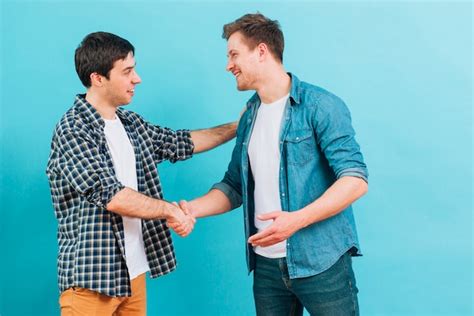 Two Smiling Young Men Shaking Hands Against Blue Background Photo