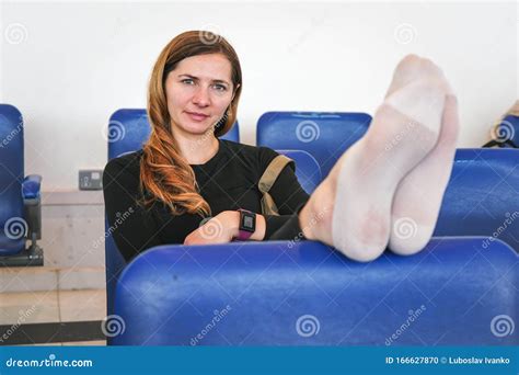 Young Tired Woman Sitting And Waiting At The Airport No Make Up Shoes Off On Seat In Front Of