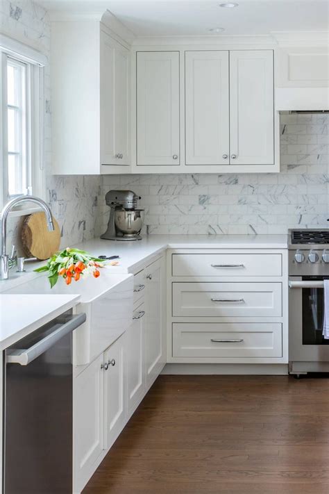 a kitchen with white cabinets and marble counter tops an oven and dishwasher