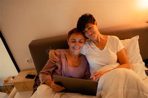 Mature Lesbian Couple Hugging And Smiling While Lying In Bed Stock