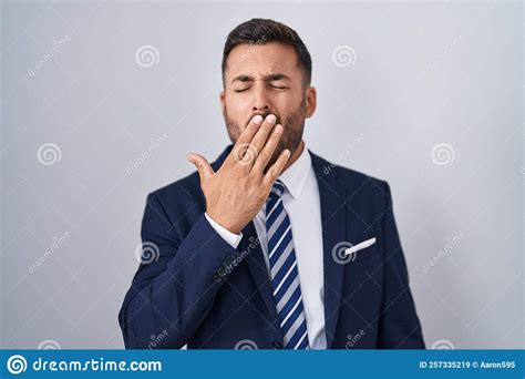 Handsome Hispanic Man Wearing Suit And Tie Bored Yawning Tired Covering Mouth With Hand Stock