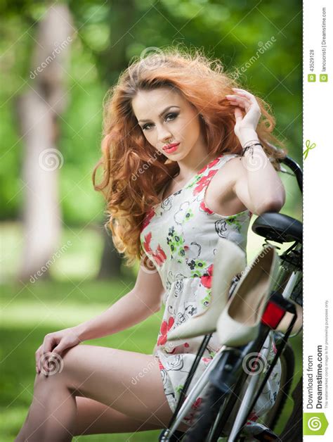 Beautiful Redhead Relaxing With Bicycle In The Summer Park