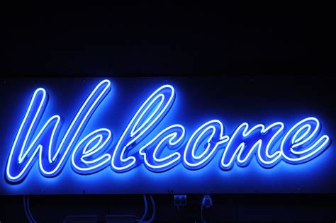 A Welcome Sign Lit Up In The Dark With Neon Lights On Its Side