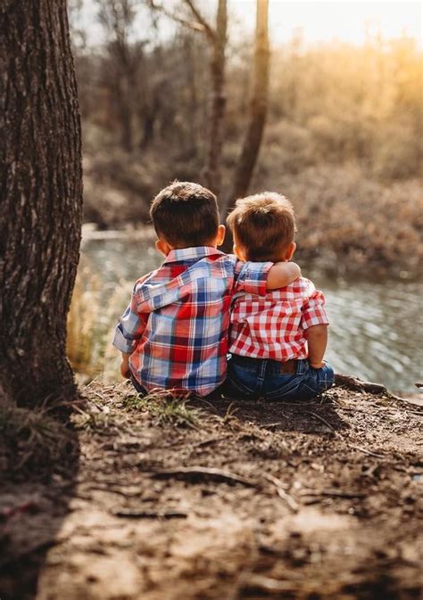 Two Young Boys Sitting Next To Each Other On The Ground Near A Tree And