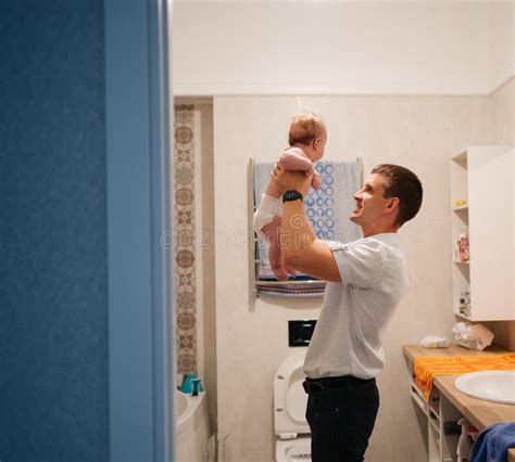 Dad Plays With Newborn Son And Tosses Him Up In The Bathroom Water Procedures Stock Photo