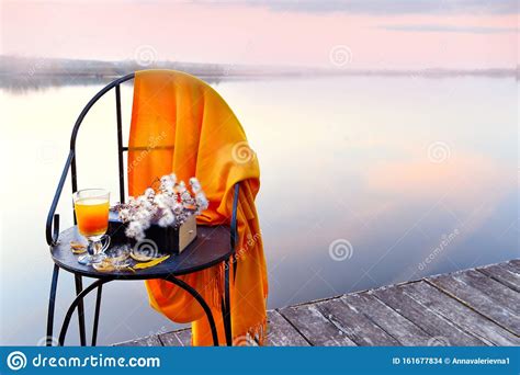 A Chair With Sea Buckthorn Tea And A Book On The Shore Of A Calm Lake