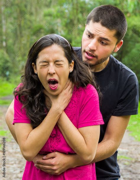 Young Woman Choking With Man Standing Behind Performing Heimlich Maneuver Park Environment And