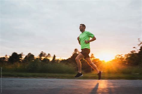 Motivated Young Man Running Up Hill Outside At Sunset By Stocksy