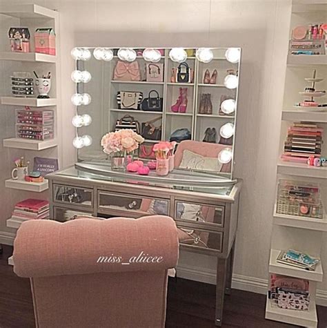 A Pink Chair Sits In Front Of A Vanity With Lights On It And A Large