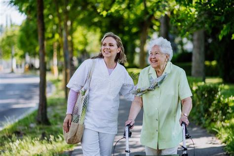 Portrait Of Caregiver With Senior Woman On Walk In Park With Shopping
