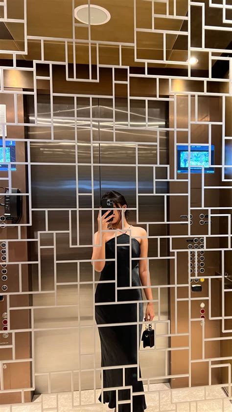 A Woman Standing In Front Of A Mirror Holding A Cell Phone
