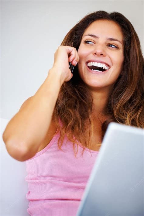 A Woman Smiles As She Talks On Her Cell Phone While Using A Laptop Computer In Front Of Her