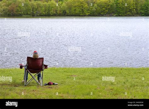 Lone Man Sleeping On A Folding Chair By The Grassy Shore Of A River