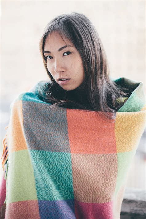 beautiful asian woman wrapped in colored blanket looking at camera by stocksy contributor