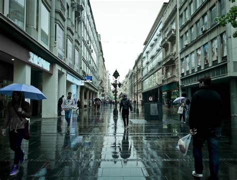 People Are Walking Down The Street With Umbrellas