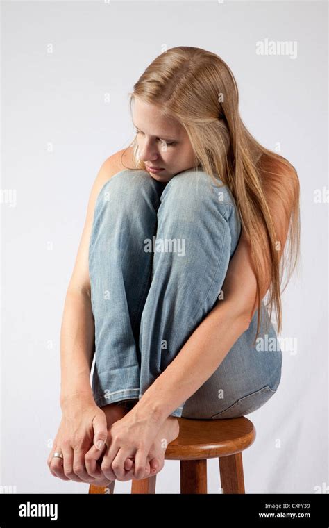 Lovely Blond Woman Sitting With Her Knee Raised Up Near Her Chin Looking At The Camera With A