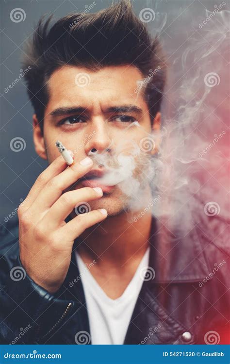 Trendy Attractive Man Blowing Smoke Out Of His Mouth Standing On Grey