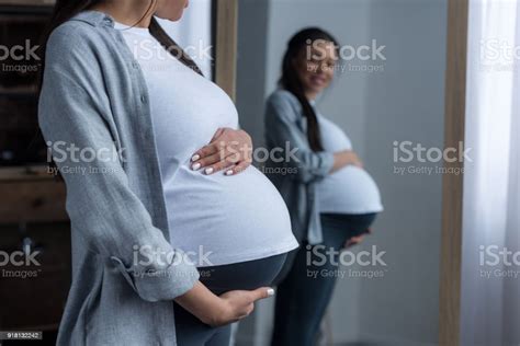 African American Pregnant Woman Looking At Her Belly In Mirror Stock