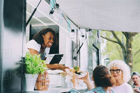 Female Owner Giving Indian Food To Smiling Customers In City Stock Photo Dissolve