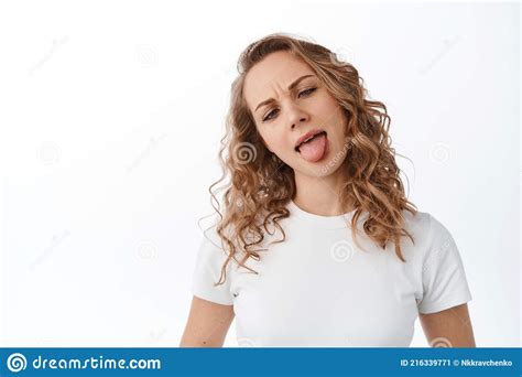 Funny Blond Girl Showing Tongue And Silly Faces Squinting Eyes Standing Against White