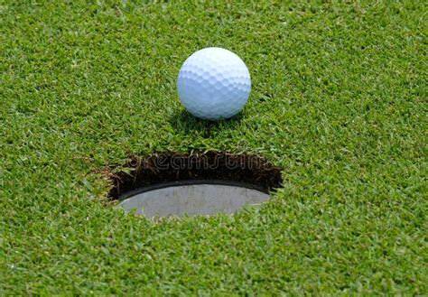 A Golf Ball On A Golf Green Sitting At The Edge Of The Hole Stock Photo