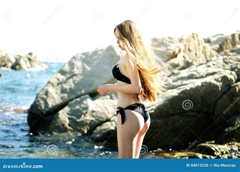 Girl In Black Bikini With Figure Standing Near Rocks Stock Photo