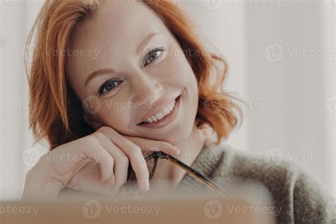 close up shot of happy beautiful redhead woman tilts head smiles positively has white perfect